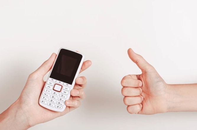 Person holding a dumbphone, another person giving a thumbs up