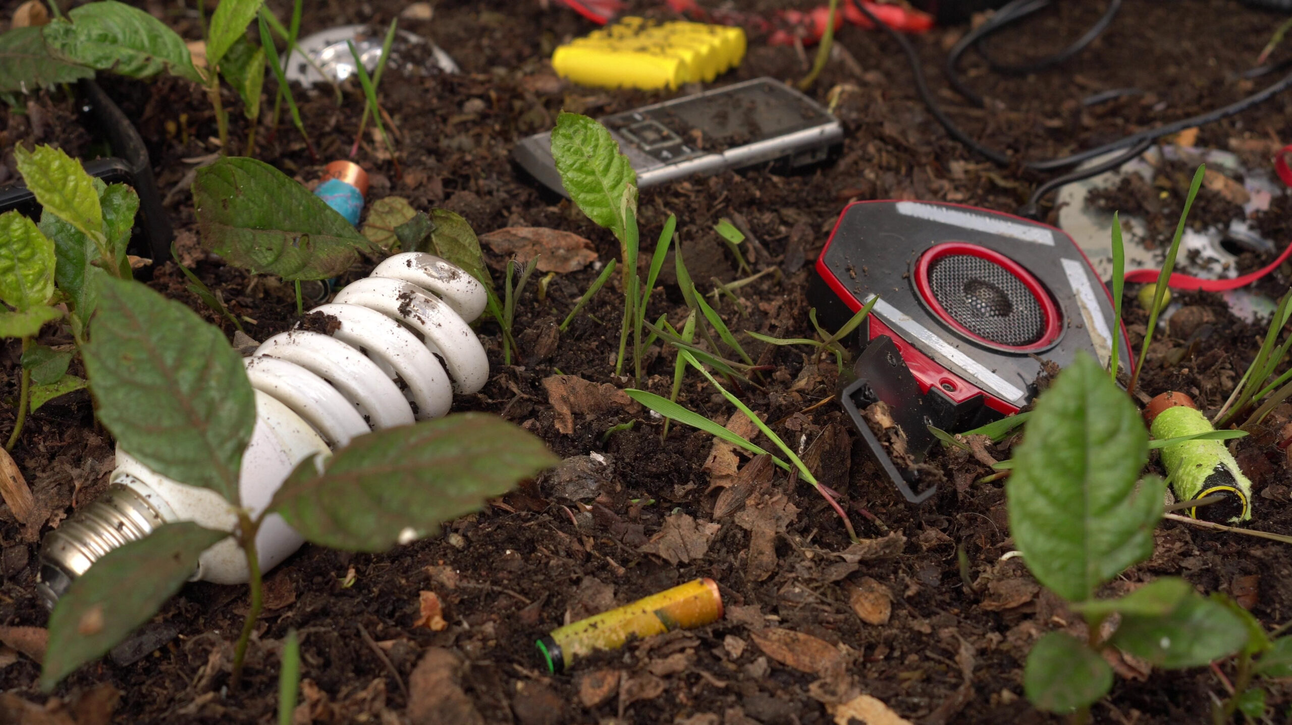 Tech in dirt with plants, e-waste, landfill