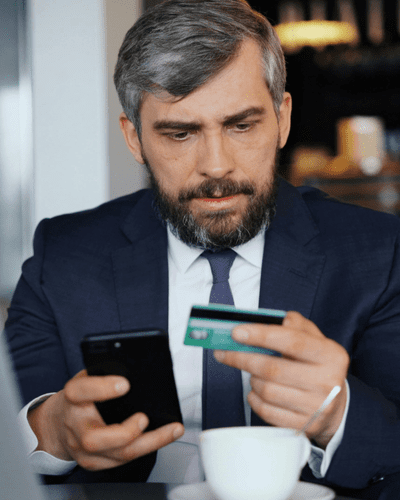Man checking bank card in one hand and refurbished phone in other
