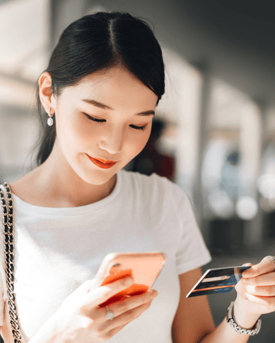 Woman admiring refurbished phone in one hand and bank card in the other