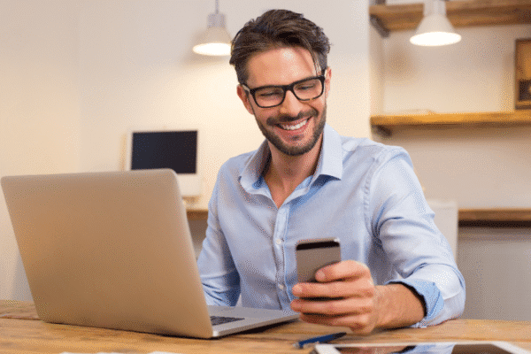 Man smiling at refurbished phone with laptop on desk