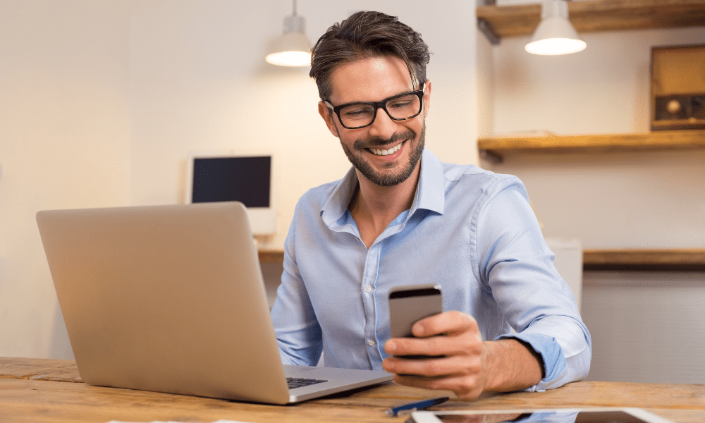 Man smiling at refurbished phone with laptop on desk